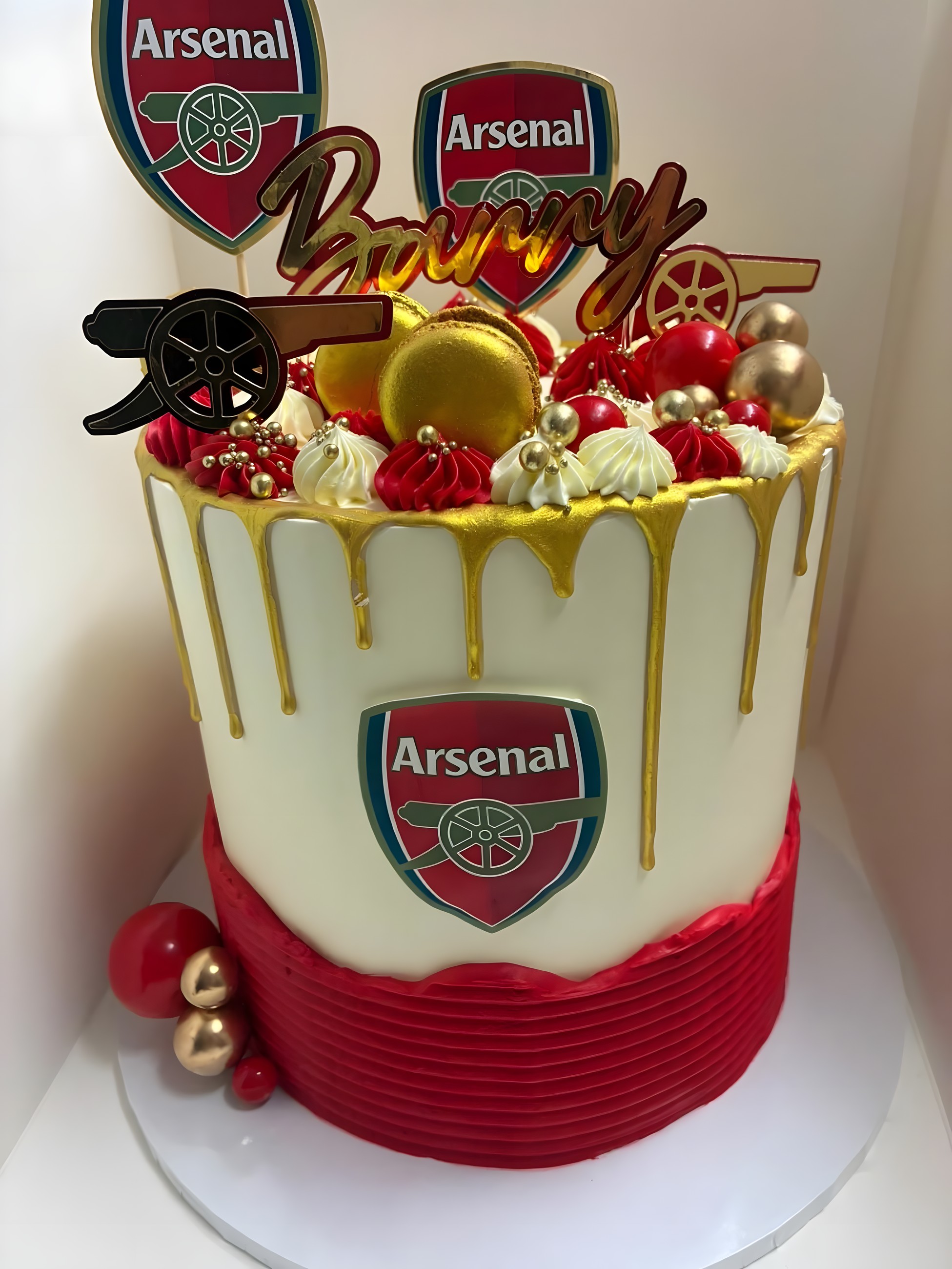 A white and red cake with a gold drip and Arsenal football crests