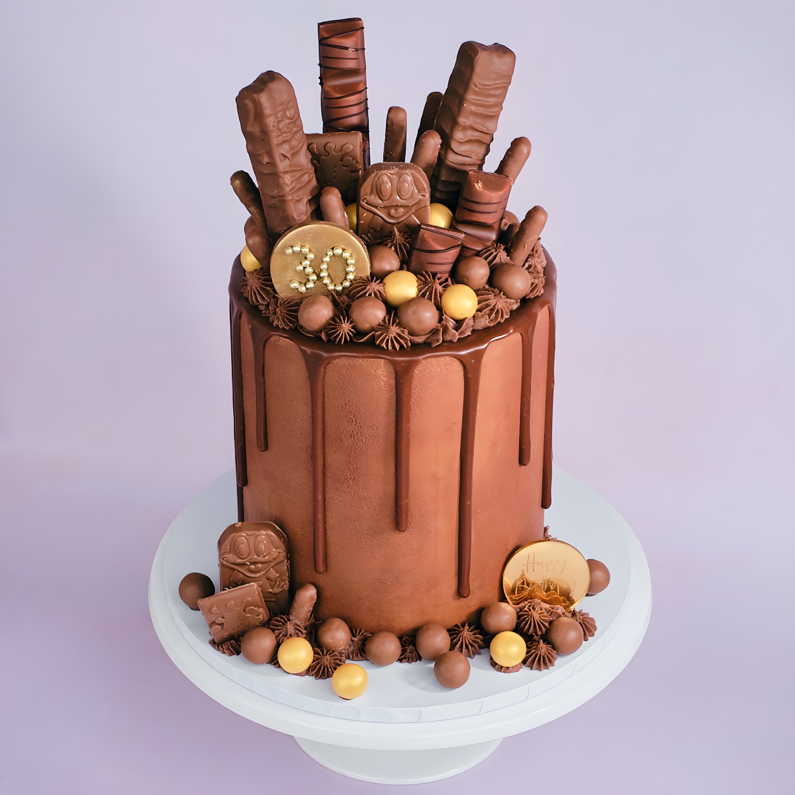 A tall chocolate drip cake loaded with chocolate bars, gold balls and a gold 30 plaque
