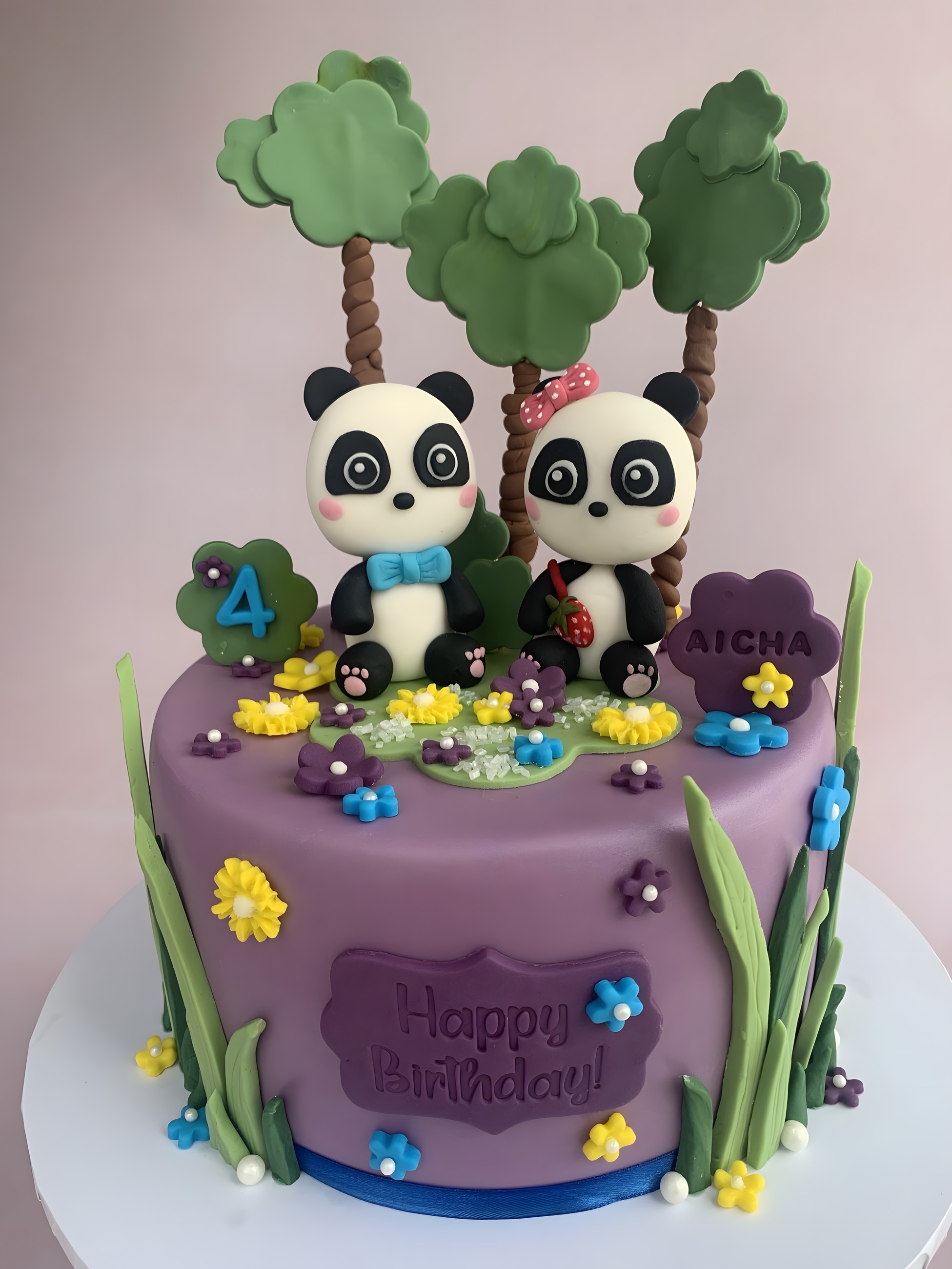 A purple fondant cake with hand-modelled panda figures, trees and flowers for a fourth birthday