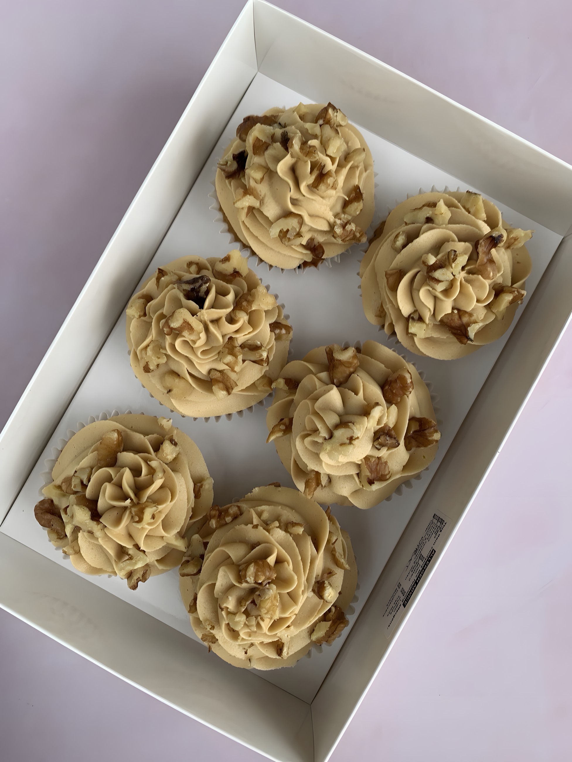 A boxed set of coffee buttercream cupcakes topped with walnut pieces