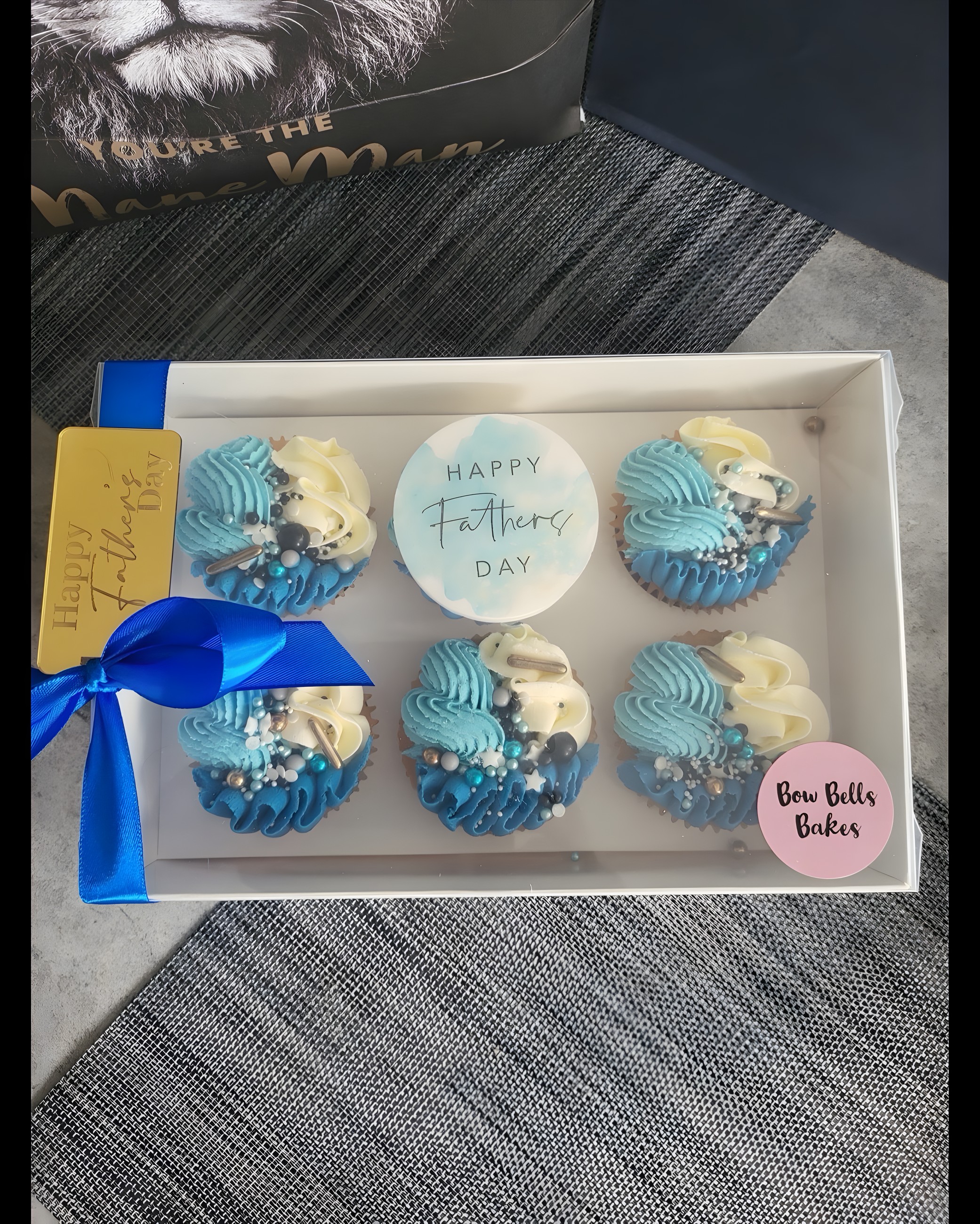 A boxed set of blue and white piped cupcakes with a Bow Bells Bakes label