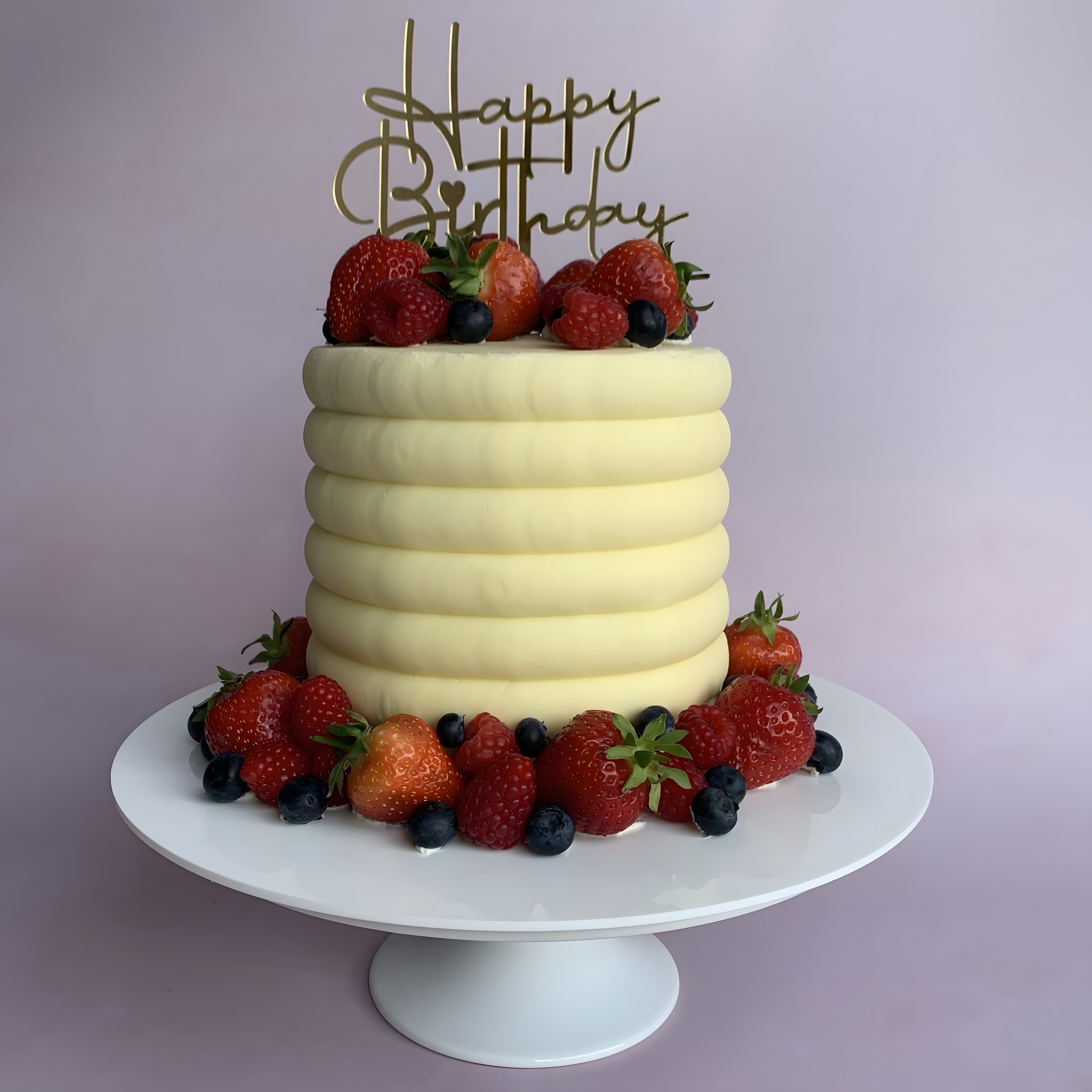 A white buttercream celebration cake ribbed by hand and topped with fresh strawberries, raspberries and blueberries, made by Bow Bells Bakes
